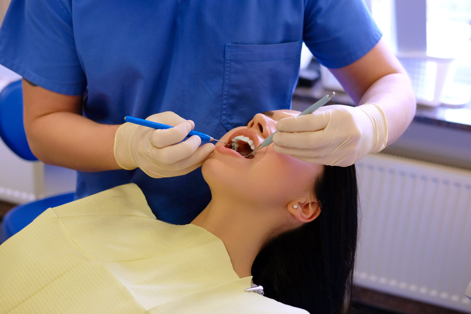 Dentist hands working on young woman patient with dental tools.