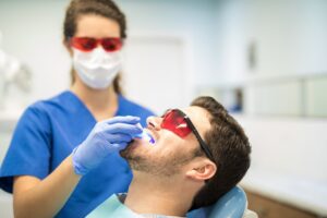 Dentist Checking Man With Ultraviolet Light In Clinic